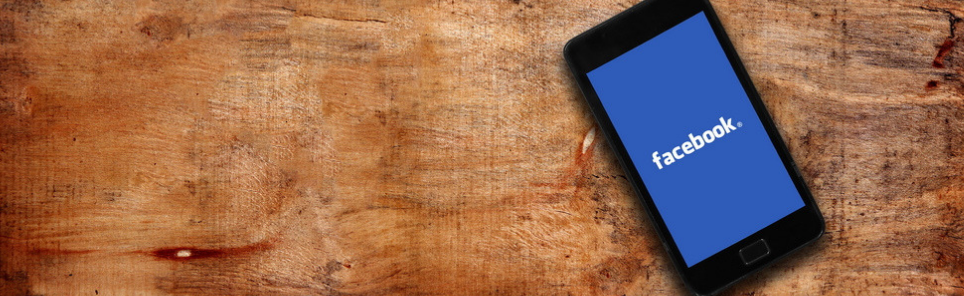 Smartphone with Facebook logo on screen lying on a wooden surface.