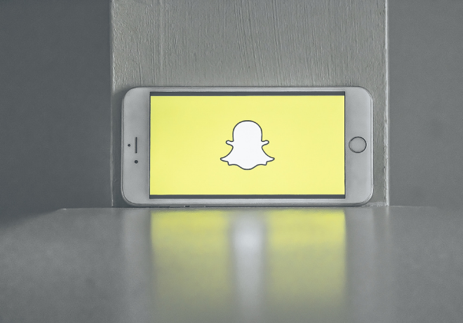 A smartphone displaying the Snapchat logo on its screen, with a desaturated background emphasizing the logo's color.