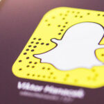 Close-up of a person's hand holding a smartphone displaying the Snapchat app logo on the screen.