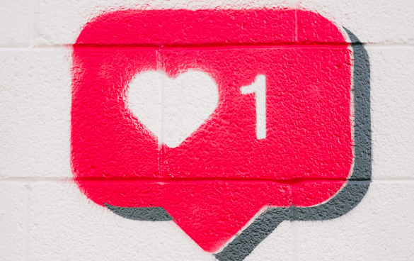 Graffiti of a red social media 'like' notification icon with a heart and the number one on a white brick wall.