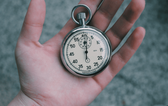 A hand holding an analog stopwatch with the second hand near the 60-second mark.