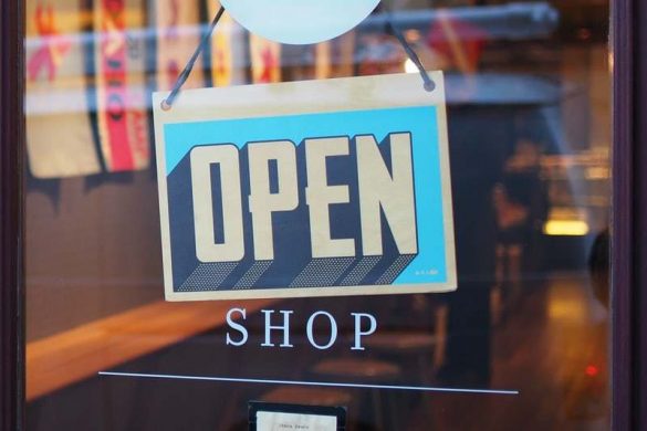 An 'OPEN' sign with a blue and white design hanging on a shop's glass door, indicating the shop is open for business.