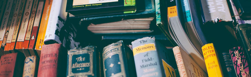 A close-up of a diverse collection of books with colorful spines, some upright and others stacked, showcasing a variety of titles and authors.