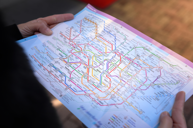 Person holding a detailed, colorful subway map with various lines and station names.