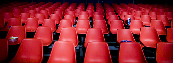 Rows of empty red seats in an indoor theater or auditorium with a popcorn box and a drink cup left on a couple of seats.