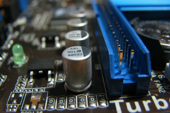 Close-up of a computer motherboard featuring a capacitor, a blue PCI Express slot labeled 'Turbo', a green LED, and various other electronic components.