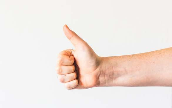 A person's hand giving a thumbs up sign against a white background.