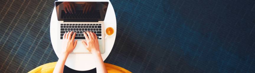 Overhead view of a person in a yellow outfit typing on a laptop with a cup of coffee on a white table against a dark blue textured background.