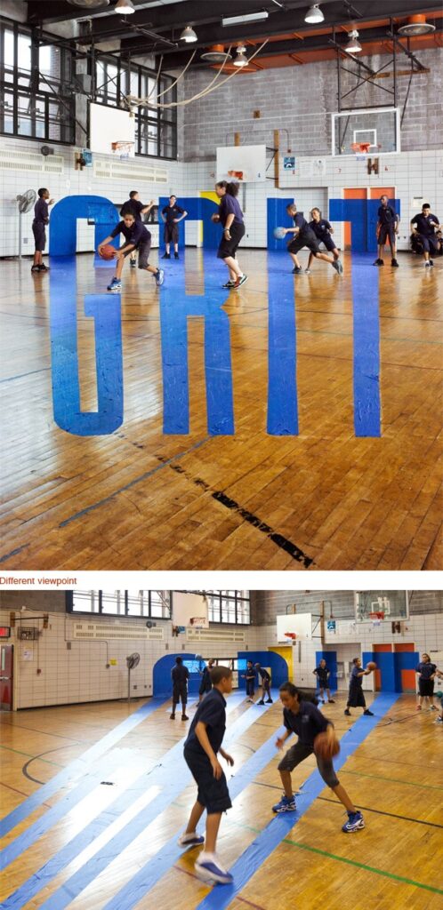 Two photos of a gymnasium with people playing basketball. The top photo shows an optical illusion of the word 'GRIT' standing upright on the floor from a specific angle, while the bottom photo shows the same scene from a different angle where the painted letters are distorted and the illusion is not present.