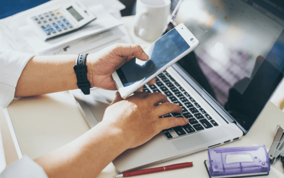 Person working on a computer and browsing on their phone.