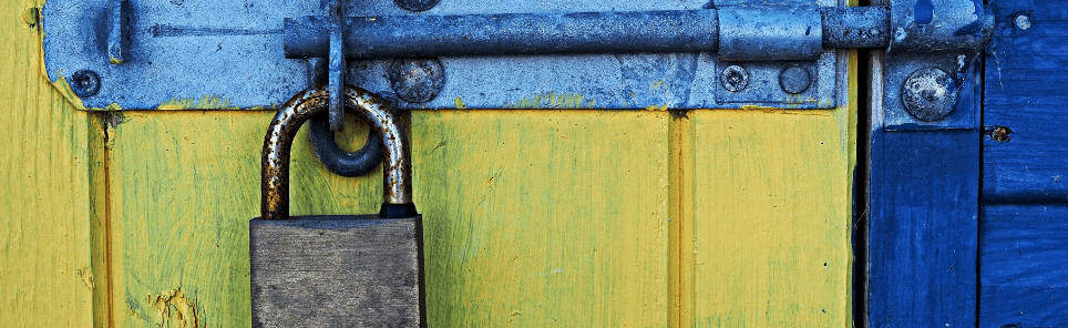 A weathered padlock secures a metal latch on a wooden door painted half yellow and half blue.