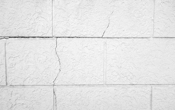 Close-up of a white textured wall with a diagonal crack across the blocks.