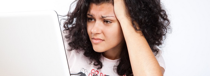 Concerned woman with curly hair looking at a laptop screen with her hand on her forehead.