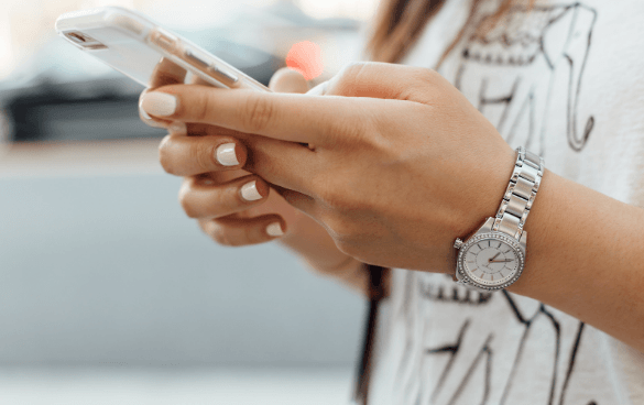 Close-up of a person's hands holding a smartphone with a silver watch on the wrist.