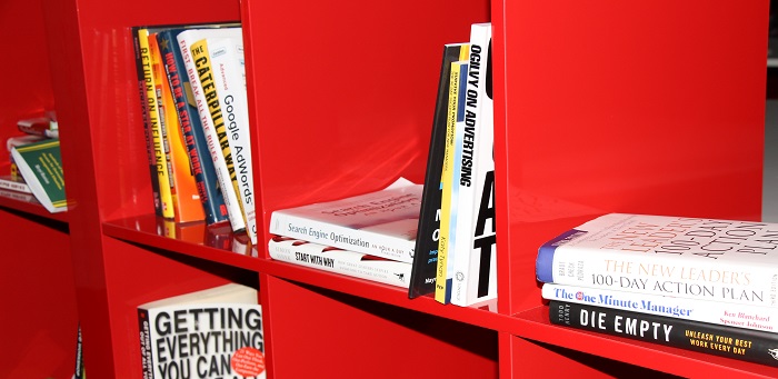 A red bookshelf filled with books on leadership, management, and personal development, with some titles visible.