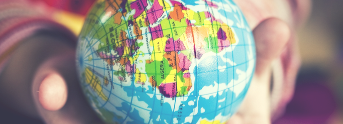 Close-up of a person's fingers holding a small, colorful globe with a blurred background.