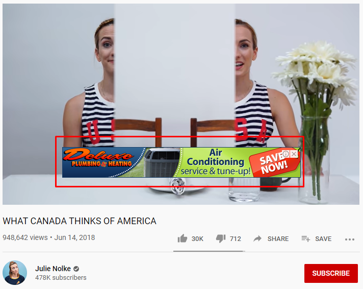 A woman in a striped tank top appears thoughtful in a YouTube video titled 'WHAT CANADA THINKS OF AMERICA' by Julie Nolke. A mirror reflects her image, and a vase with white flowers is to her right. A red banner ad for air conditioning service is displayed at the bottom, and YouTube interface elements show the video's views, likes, and other options.