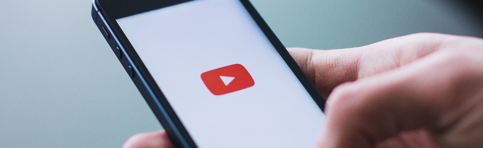 Close-up of a person's hand holding a smartphone displaying the YouTube logo on the screen.