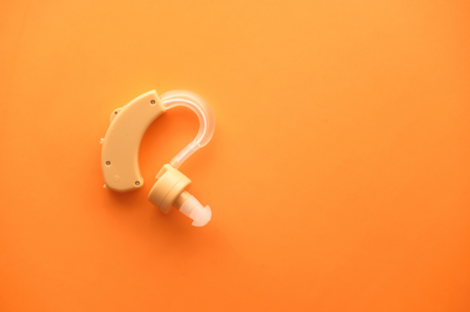 A beige hearing aid on an orange background.