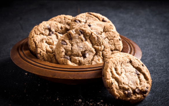 Freshly baked chocolate chip cookies on a wooden plate.