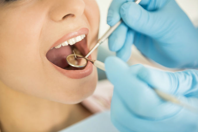 Close-up of a dental examination with a patient's open mouth showing teeth being inspected by a dentist wearing blue gloves.