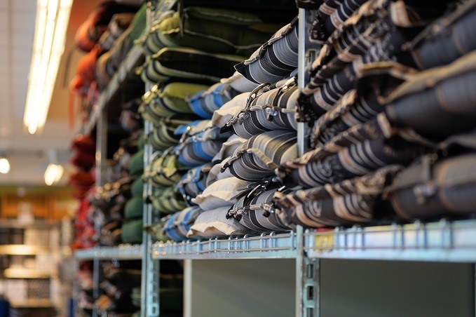 Neatly folded pants in various colors and patterns displayed on metal shelves in a retail store.