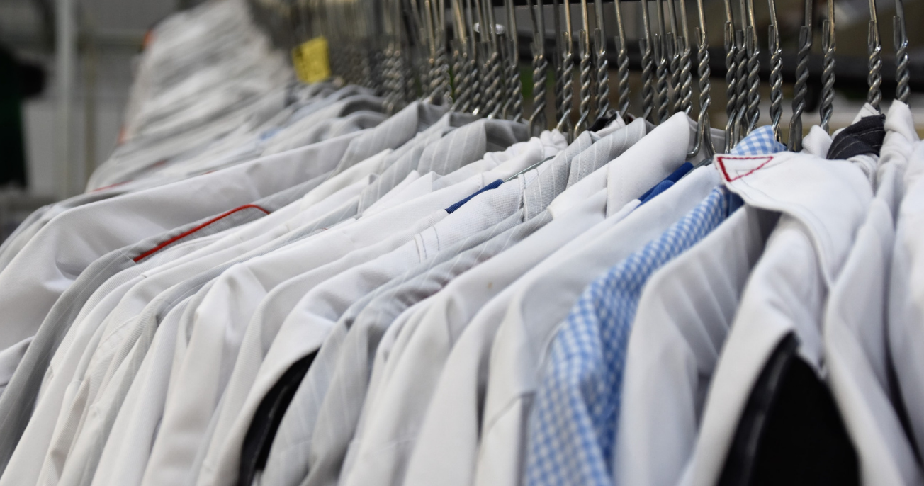 A collection of freshly laundered and pressed white and light-colored shirts hanging on a conveyor system at a dry cleaning or laundry service.