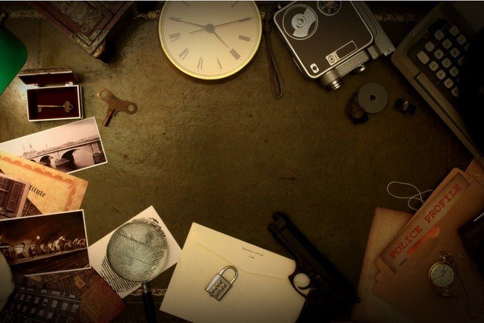 A collection of detective-themed items including a vintage camera, typewriter, handgun, handcuffs, magnifying glass, pocket watch, rotary dial telephone, keys, fingerprint, police folder, and black and white photographs on a dark surface.