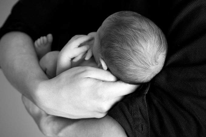 A black and white image of a newborn baby cradled in an adult's hands, with the baby appearing to be sleeping peacefully.