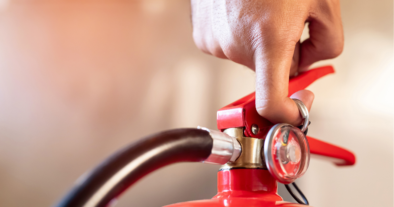 Close-up of a hand pulling the safety pin from a red fire extinguisher with a visible pressure gauge.