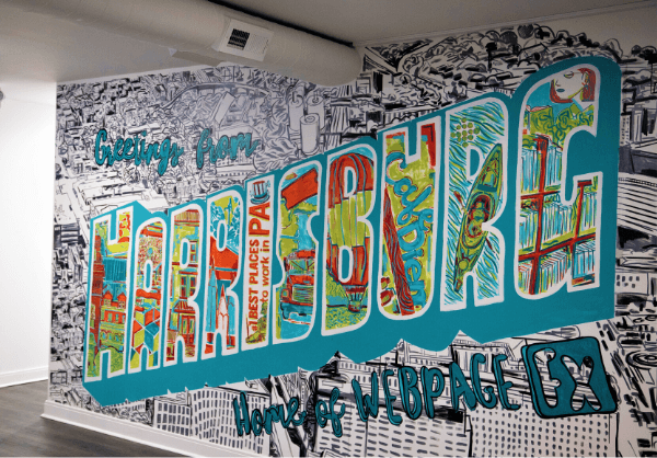 A vibrant mural with the word 'HARRISBURG' in stylized letters filled with colorful patterns and city illustrations, with 'Greetings from' above and 'Home of WEBPAGEFX' below, set against a black and white cityscape background.