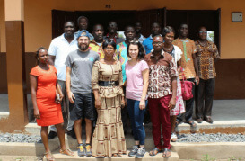 A diverse group of people smiling for a group photo in front of a single-story building.