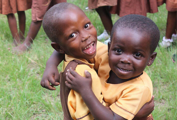 Two joyful children in yellow school uniforms hugging each other, with one child smiling broadly at the camera.