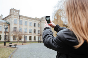 Person from behind taking a photo of a grand building with a smartphone in an outdoor setting.