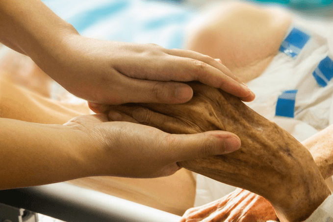 A younger person's hand gently holding an elderly person's hand on a hospital bed, conveying care and comfort.