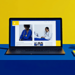 A laptop on a blue desk displays medical images, with blue and yellow office supplies and a yellow background wall.