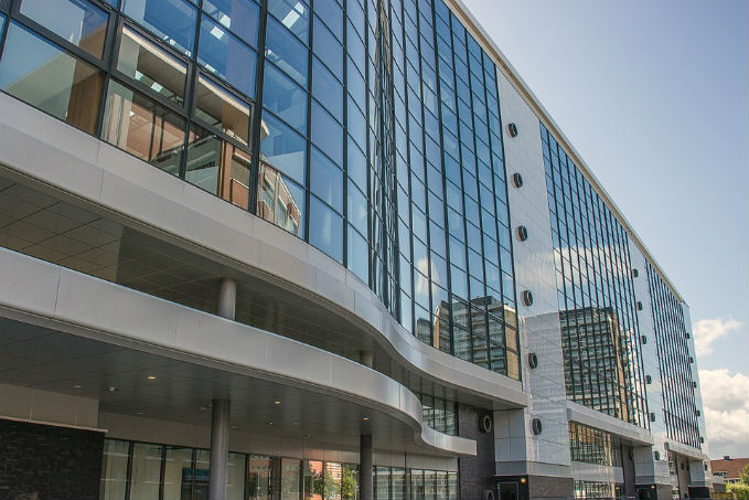 Modern multi-story building with a curved glass facade and solid panels, under a partly cloudy sky.