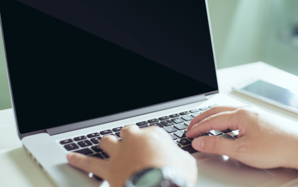 Person typing on a laptop with a black screen, wearing a watch on their left wrist, with an out-of-focus background.