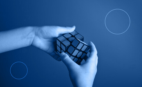 Two hands holding a Rubik's Cube with a monochromatic blue filter, alongside two outlined circles on a blue background.