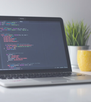 Laptop on a desk displaying code on the screen with a plant and a yellow mug in the background.