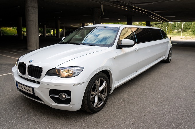 A white BMW X6 stretched limousine parked in a covered parking area.