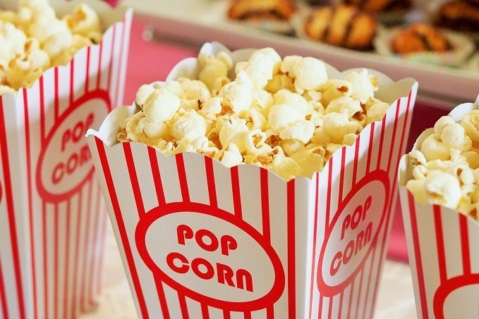 Multiple boxes of freshly popped popcorn in red and white striped containers with 'POP CORN' text, with a blurred background suggesting a party or movie setting.