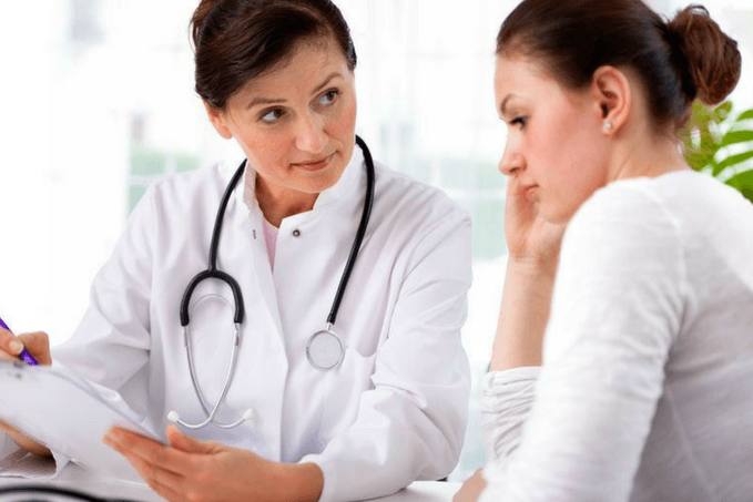 A female doctor in a white lab coat with a stethoscope discussing a document with a concerned female patient in a medical office.