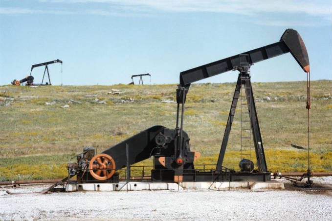 Oil pump jacks, also known as nodding donkeys, in a grassy field with a clear sky.