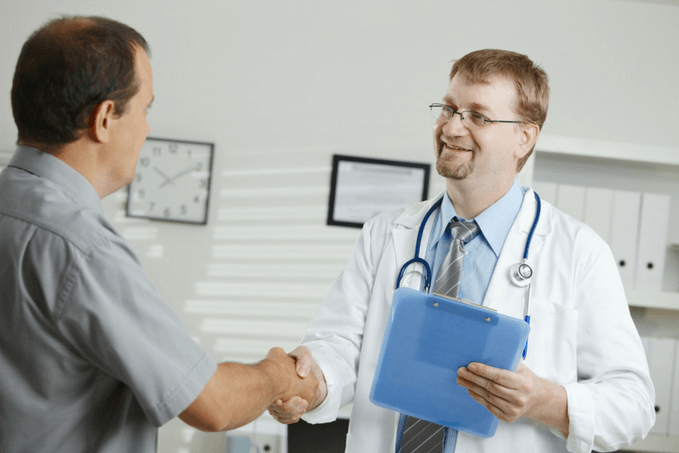 A doctor in a white lab coat with a stethoscope shaking hands with a man in a gray shirt in a medical office.