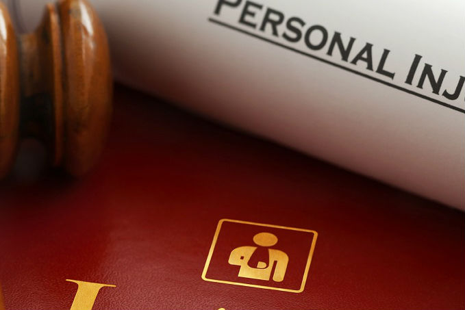 A wooden gavel on a red-brown leather surface with a document labeled 'PERSONAL INJURY' and a golden pictogram of a person with a cast on one leg, symbolizing personal injury law.