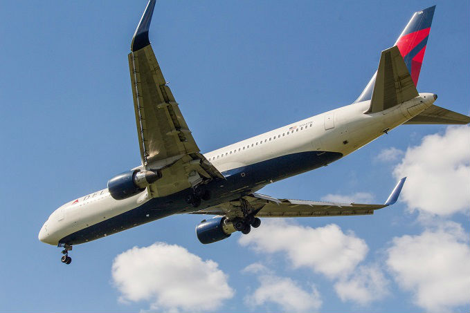 A commercial airliner in flight against a blue sky with some clouds, featuring the tail logo of Delta Air Lines.