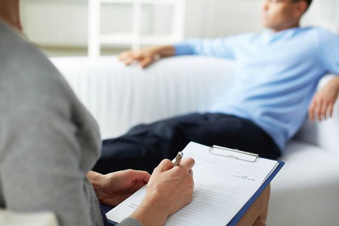 A therapist taking notes on a clipboard while a client lies on a couch, suggesting a counseling session.