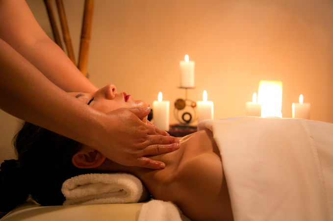 A woman receiving a facial massage in a serene spa setting with dim lighting and multiple lit candles.