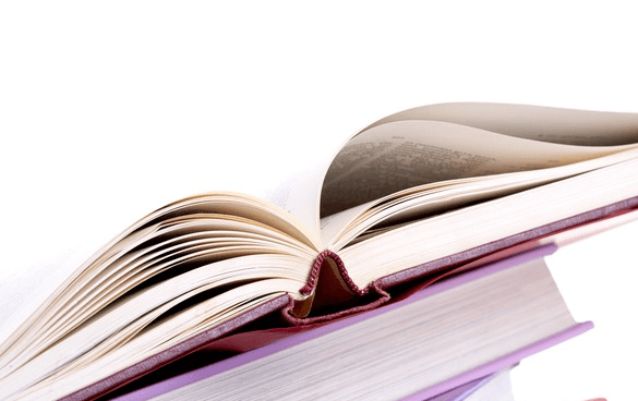 A stack of hardcover books with one book open on top, showing curved pages.